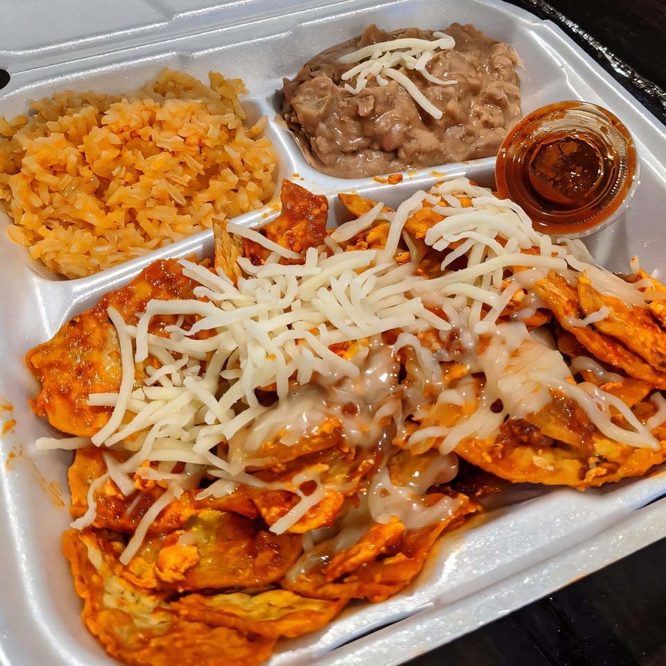 A takeout container with cheesy chilaquiles, Mexican rice, refried beans, and a side of salsa.