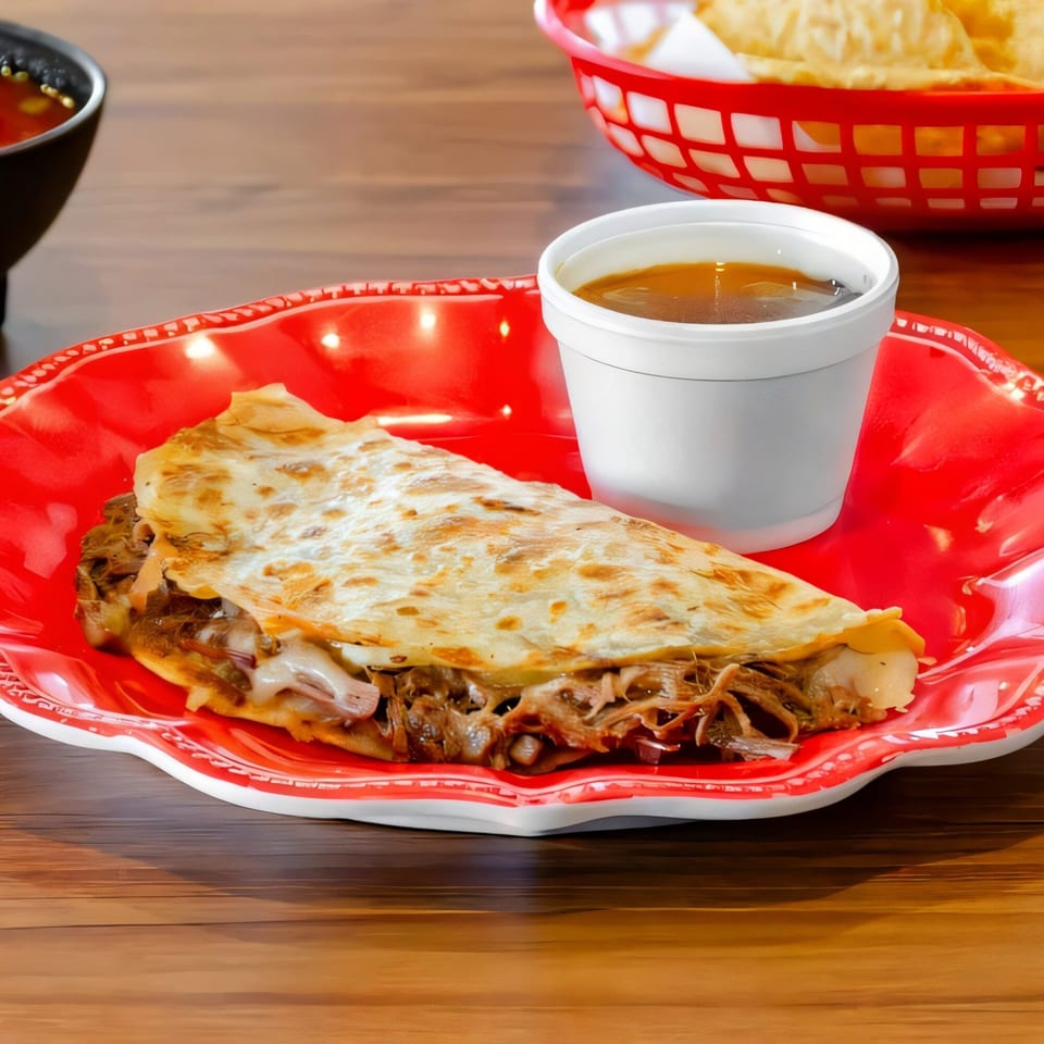 Birria quesadilla with melted cheese and shredded meat, served with a cup of consommé on a red plate.