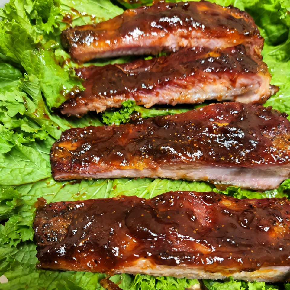 Four glazed ribs with a dark sauce, resting on a bed of bright green lettuce.