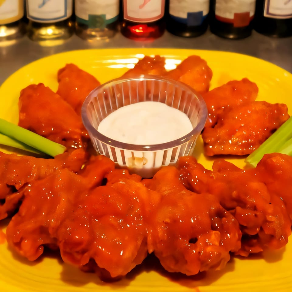 A bright yellow plate holds spicy red chicken wings, celery sticks, and a small cup of ranch dip.