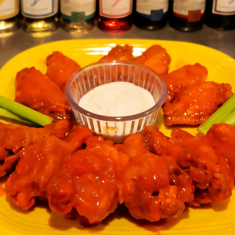 A bright yellow plate holds spicy red chicken wings, celery sticks, and a small cup of ranch dip.